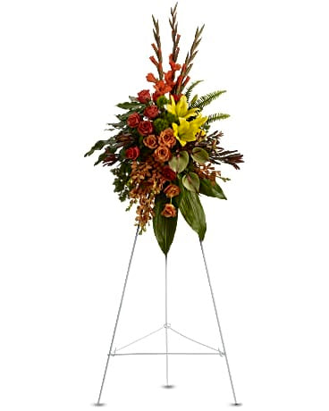 Tributo Tropical: Un elegante y moderno spray funerario de colores cálidos que incluye flores como anturios, rosas y vegetación tropical. Presentado como una exhibición de caballete de pie.